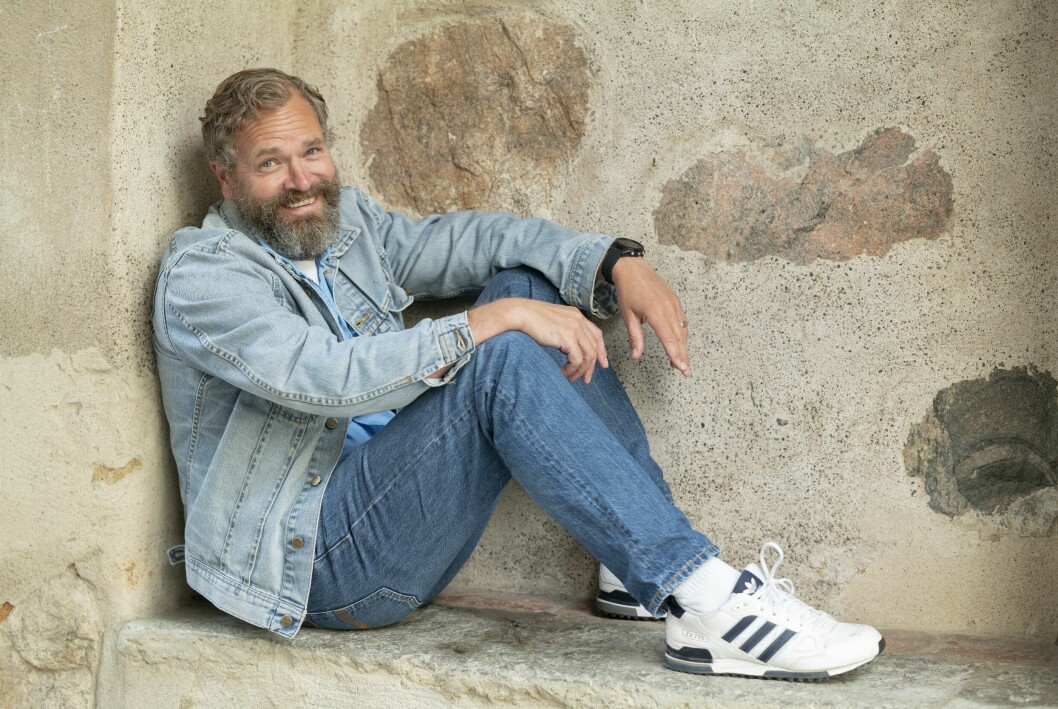 Skådespelaren Per Lasson från Tunna blå linjen sitter uppkrupen på en betongmur.