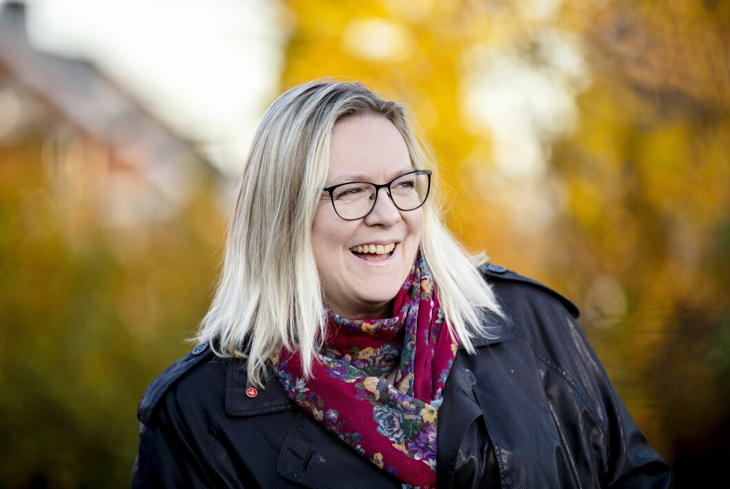 Petra låter inte sjukdomen definiera henne som person. – Min livsglädje är stor. Jag är nyfiken på livet, säger hon. Petra Hall utomhus, glatt leende och med höstgula träd i bakgrunden.