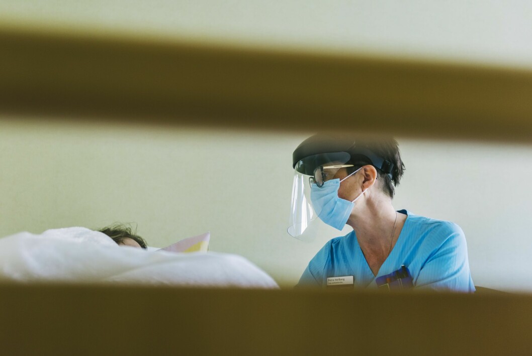 Petra Hellberg sitter med munskydd och visir intill en persons sjuksäng.