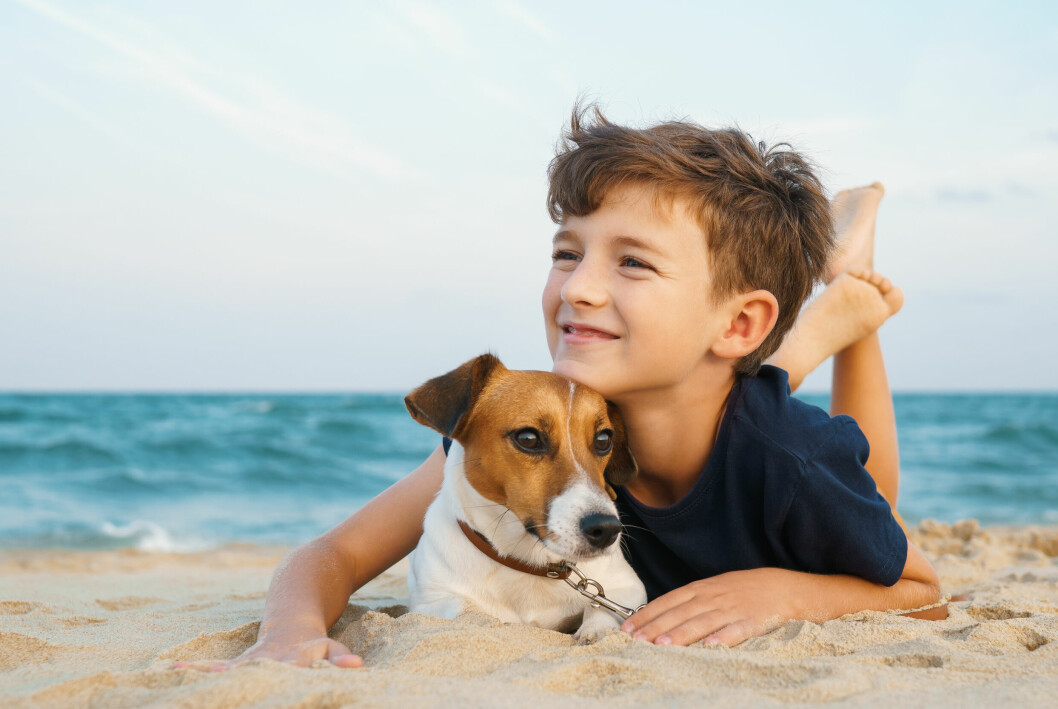 En pojke ligger på stranden och kramar om en hund.