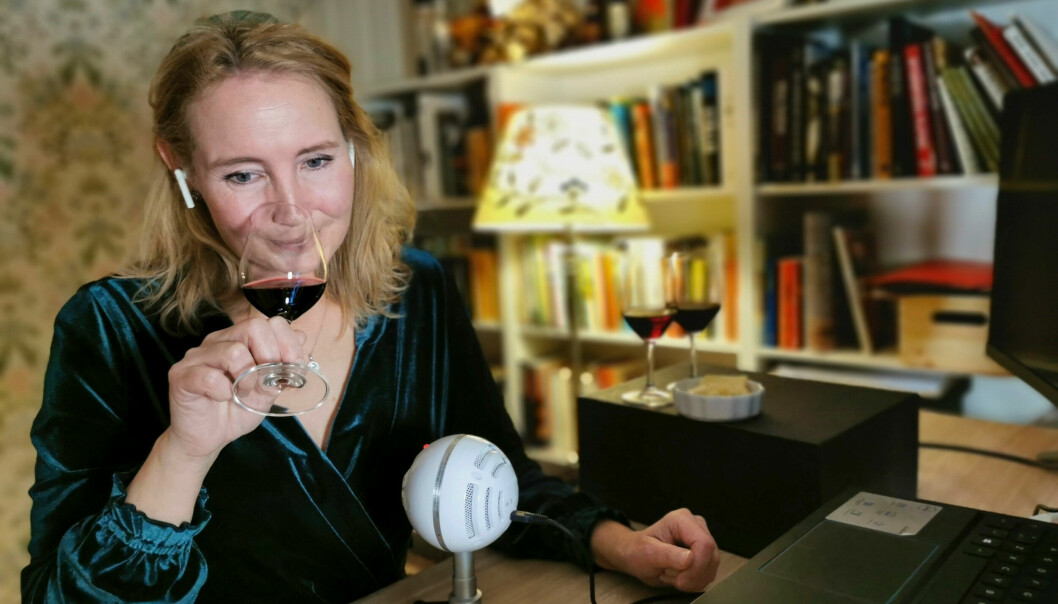 Porträttbild på Camilla och hon har på sig en sammetsklänning i mörkgrönt. Hon luktar på ett glas rödvin.