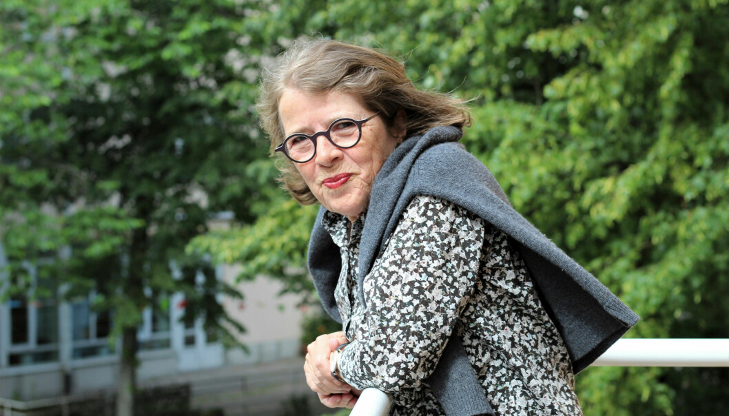 Porträttbild på Hanne. Hon lutar sig mot ett balkongräcke med gröna träd i bakgrunden.