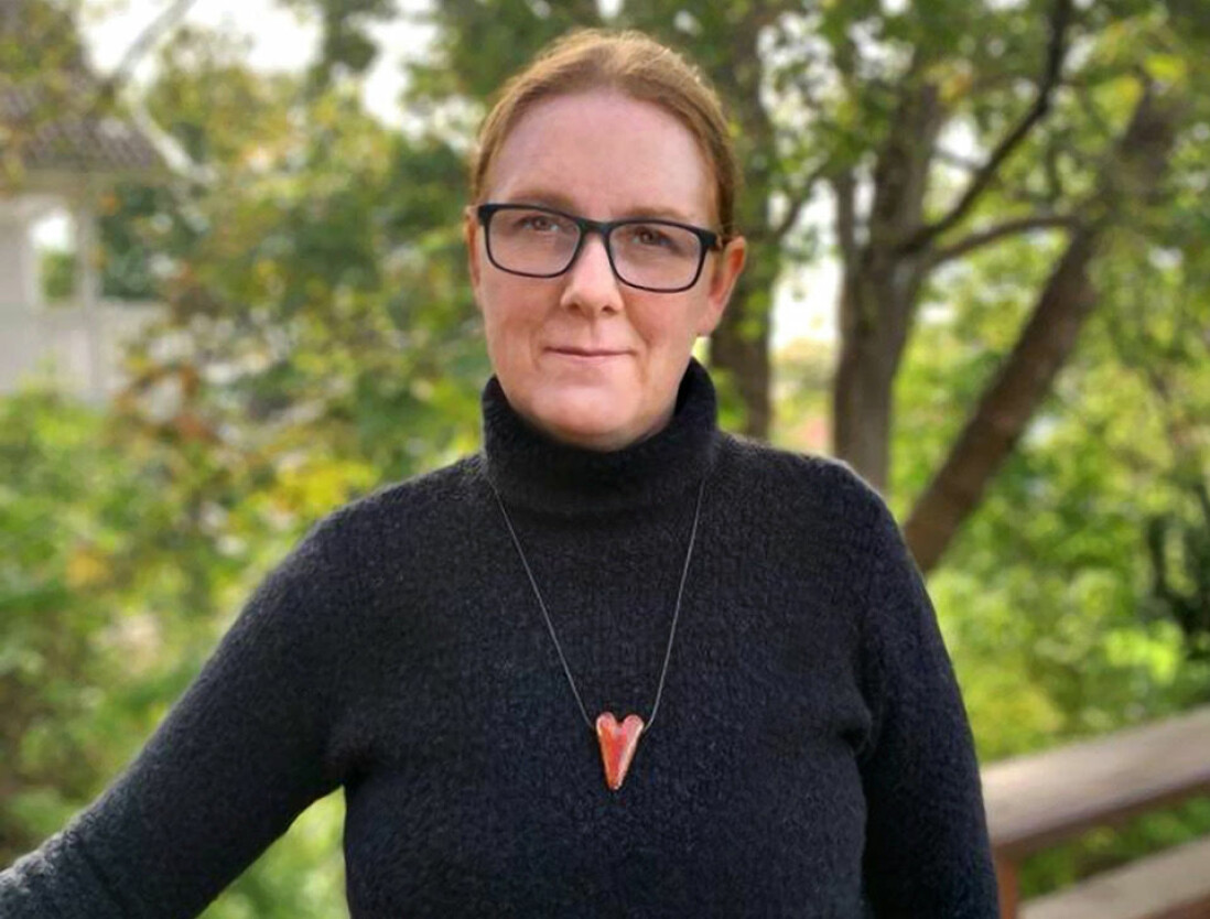 Kinna Skoglund är en av grundarna till föreningen Arbetskraftsförmedlingen, som via kampanjen Redo försöker para ihop ungdomar som hotas av utvisningen med lämpliga arbetsgivare. Porträttfoto av Kinna Skoglund, i bakgrunden syns gröna lövverk och trädstammar.