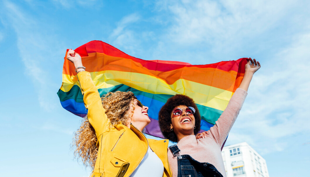 Två kvinnor ler och håller upp en Prideflagga ovanför huvudet.