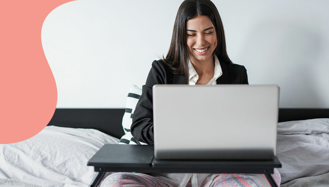 Kvinna jobbar med datorn i pyjamas i sängen.
