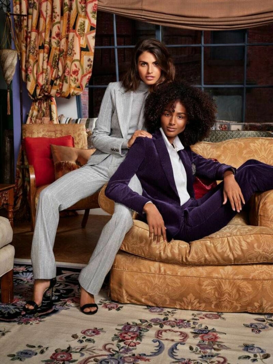 Rachel Green syntes ofta i moderiktiga statement-kostymer när hon jobbade på Ralph Lauren. Foto: Ralph Lauren Två kvinnor i Vänner-inspirerad miljö iklädda power kostymer.