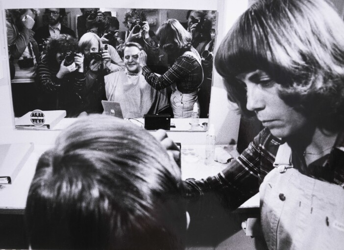 Ragnhild Haarstad och en grupp andra fotografer tar bilder av Olof Palme när han blir sminkad inför en partiledardebatt före valet 1974. Olof Palme blir sminkad inför en partiledardebatt och i spegeln framför honom syns fotografer – däribland Ragnhild Haarstad – som tar bilder av honom.