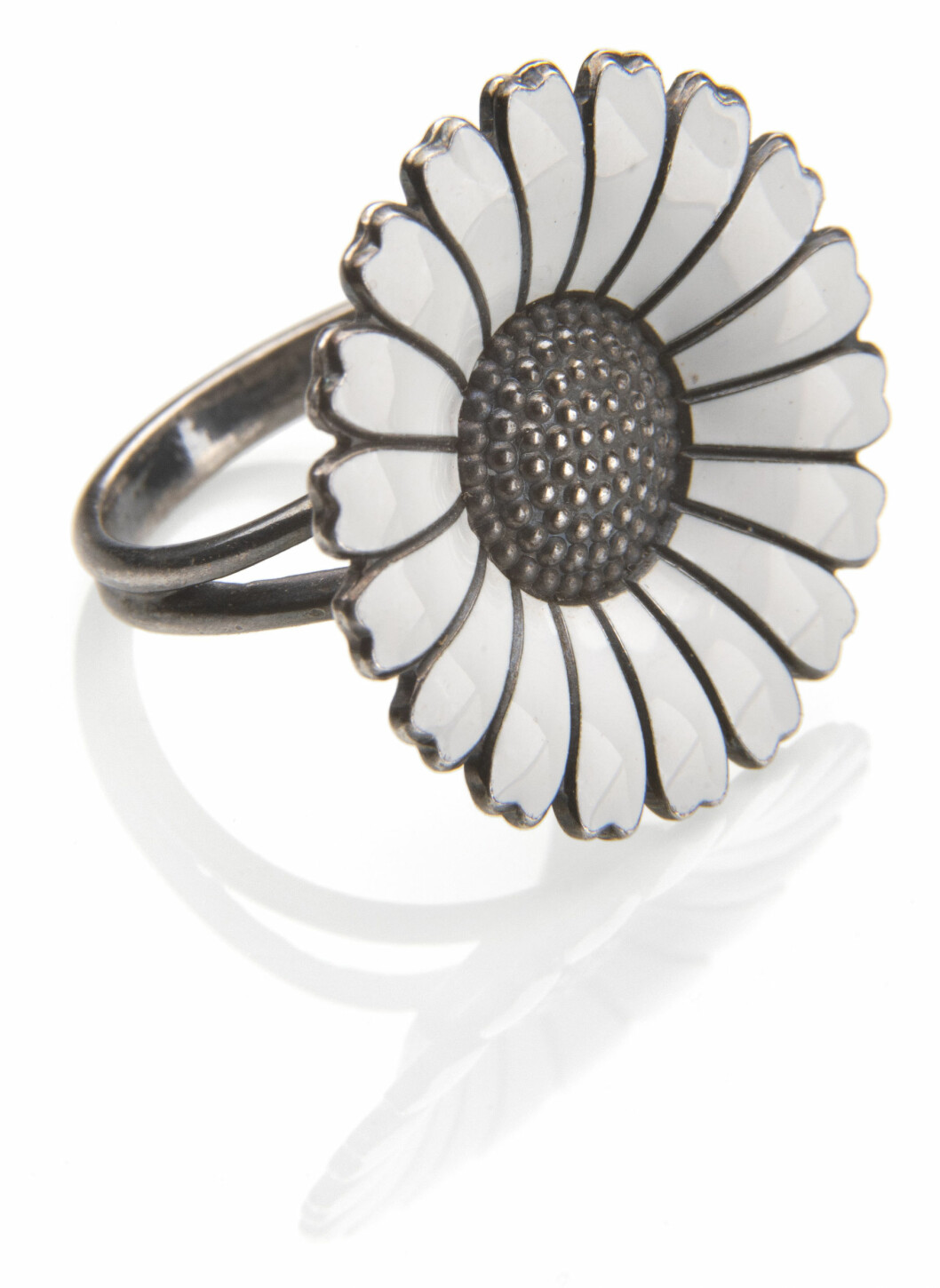 Hyllning till en blivande drottning. Margueriteringen av silver och emalj ingick i en hel smyckeserie med armband, halslänkar och örclips som den danska guldsmedsfirman Anton Michelsen presenterade 1940, efter kronprinsessan Margarethes födelse. Serien gjorde dundrande succé och producerades under många år. Ring föreställande blomma i järn och vita blad.