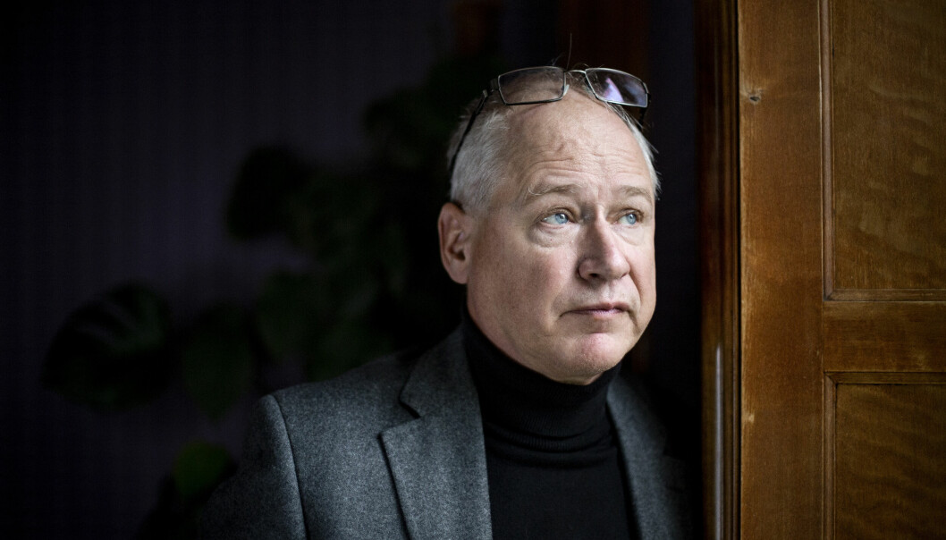 Skådespelaren Robert Gustafsson står lutad mot en fönsterkarm i trä och tittar snett framåt, som ut genom ett fönster. Han är klädd i svart polo, grå kavaj och har ett par glasögon uppe på huvudet.