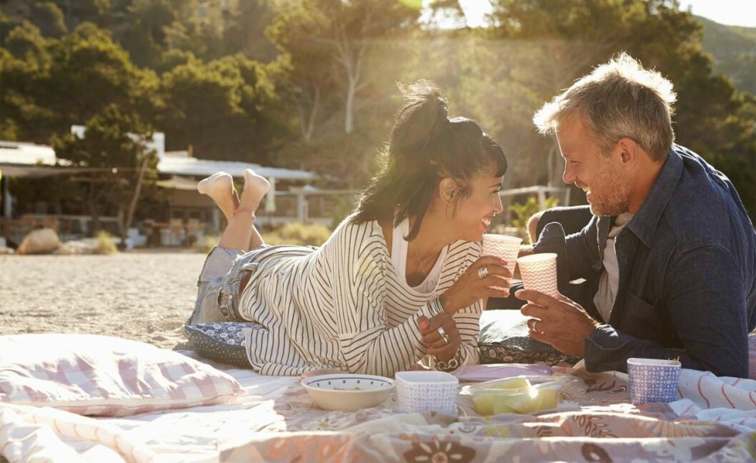 Ett kärlekspar ligger på en picknickfilt och skålar.