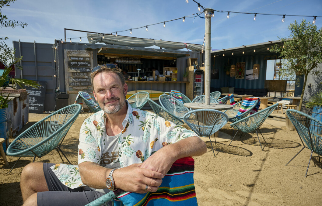 Kristofer sitter på en stol och i bakgrunden syns hans sommarrestaurang Salty dog.