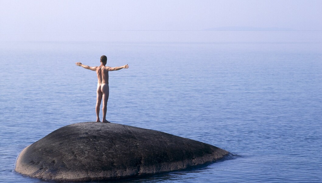 Naken man står på liten miniö på Vättern.