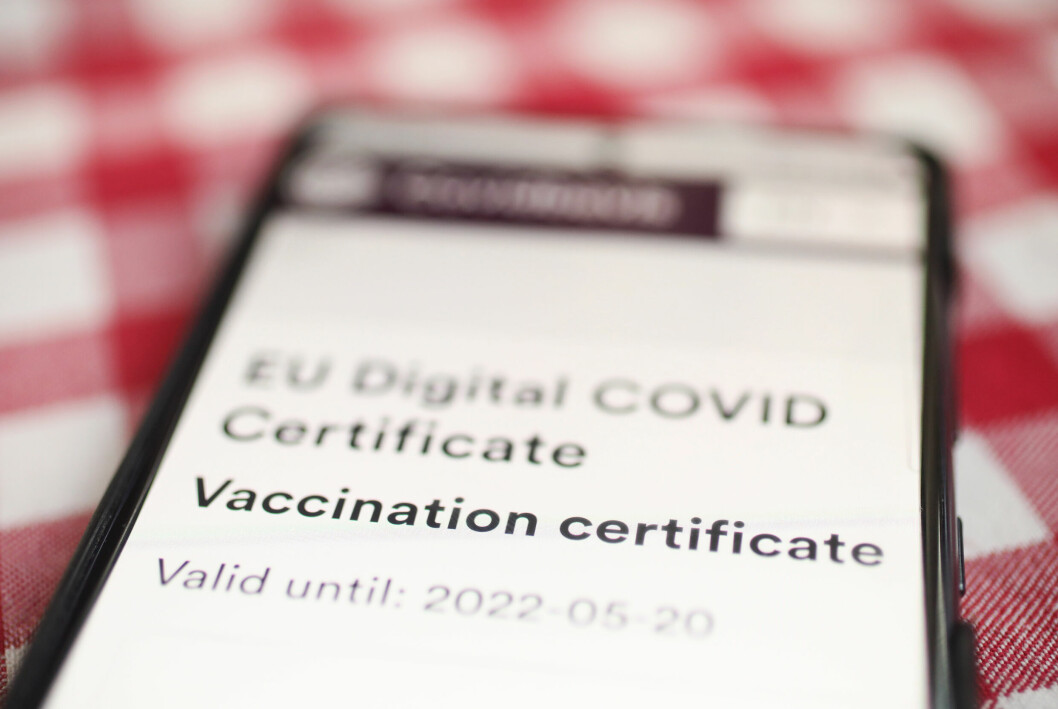 Bild på en telefon på en rutig duk, skärmen visar ett covidbevis, rubriken Vaccination certificate är i fokus men resten av bilden är suddig.