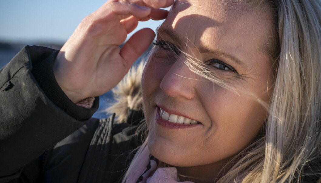Närbild av Carina Bergfeldt som ler och håller undan håret från sitt ansikte. Bilden är tagen utomhus och det verkar blåsa.