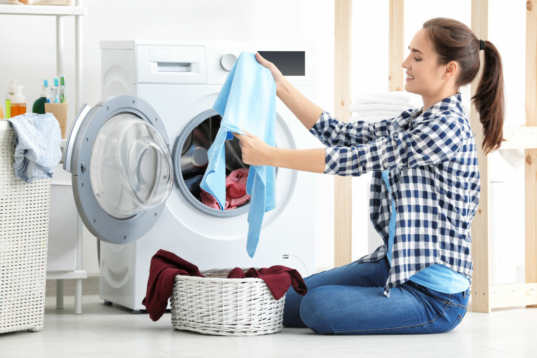 Kvinna sitter på golvet framför en tvättmaskin och tittar på ett nytvättat plagg.