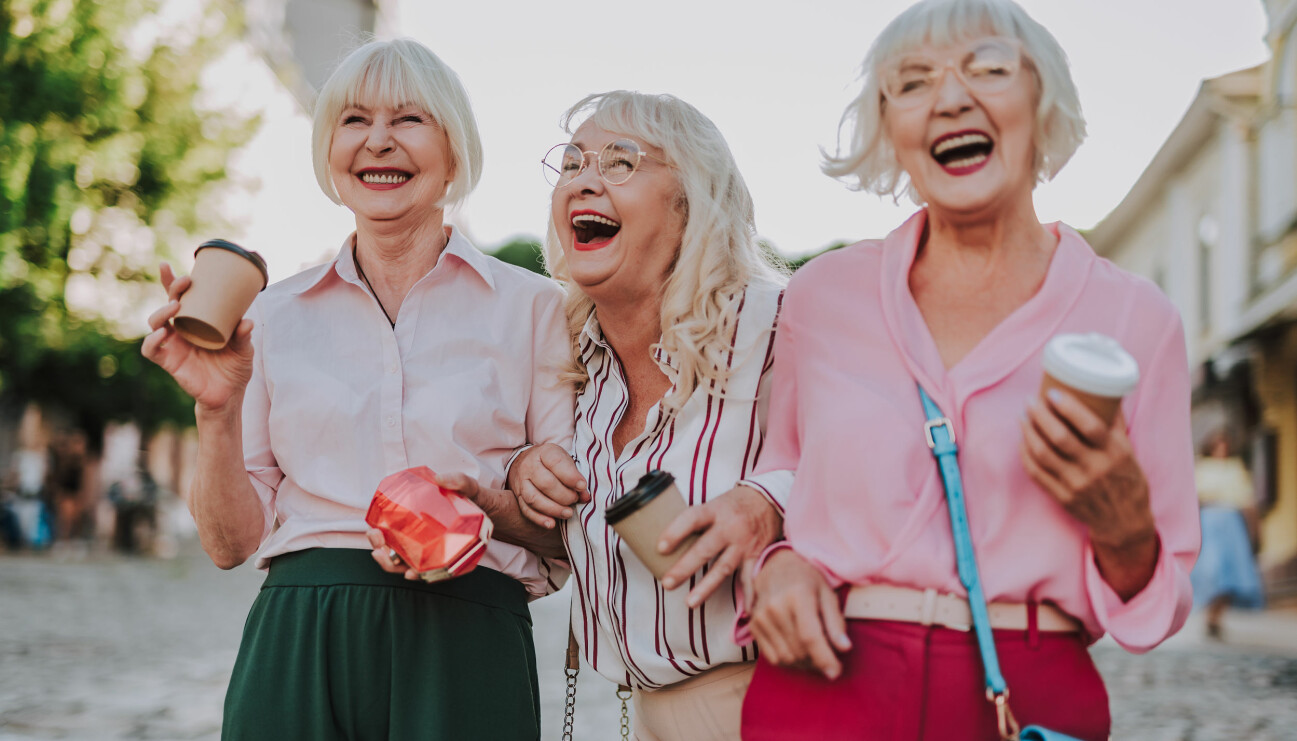 Tre äldre kvinnor skrattar, dricker kaffe och ser ungdomliga ut.