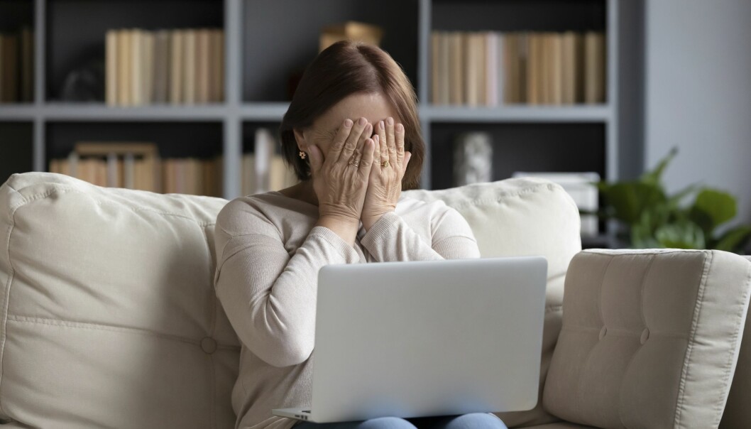 Kvinna sitter i soffan framför en laptop och håller händerna för ansiktet