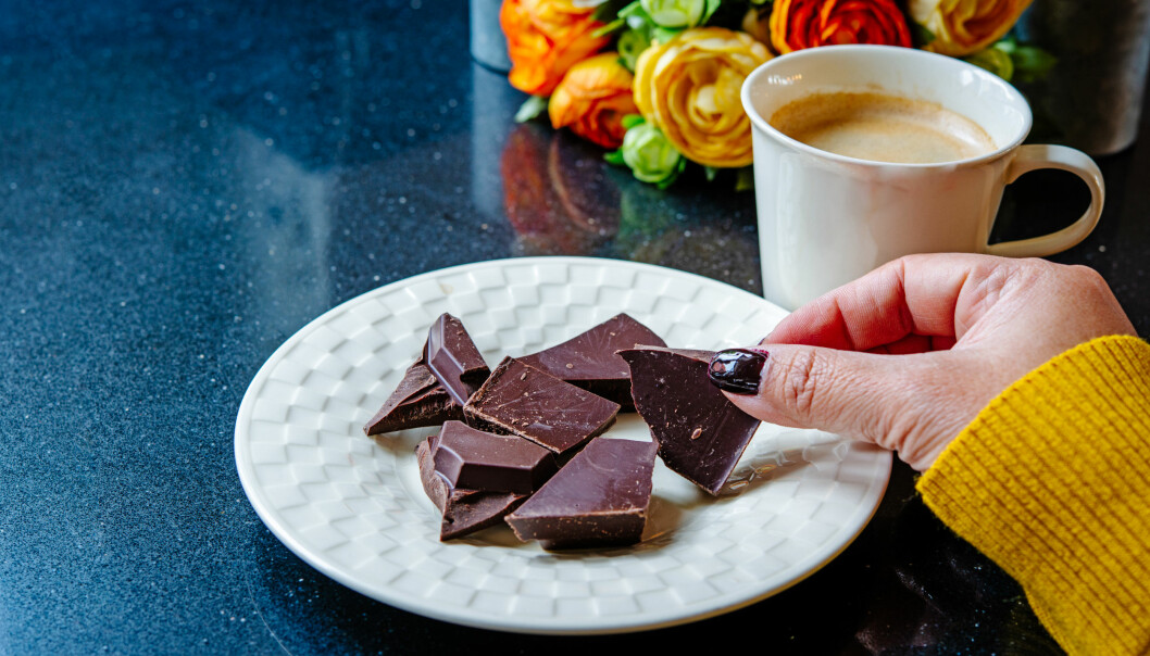 En kvinna med nagellack äter några bitar mörk choklad och dricker en kopp kaffe till.