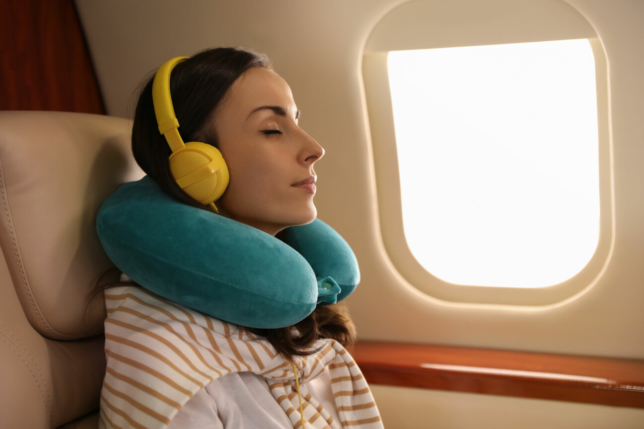 Kvinna på flygplan med nackkudde och hörlurar.