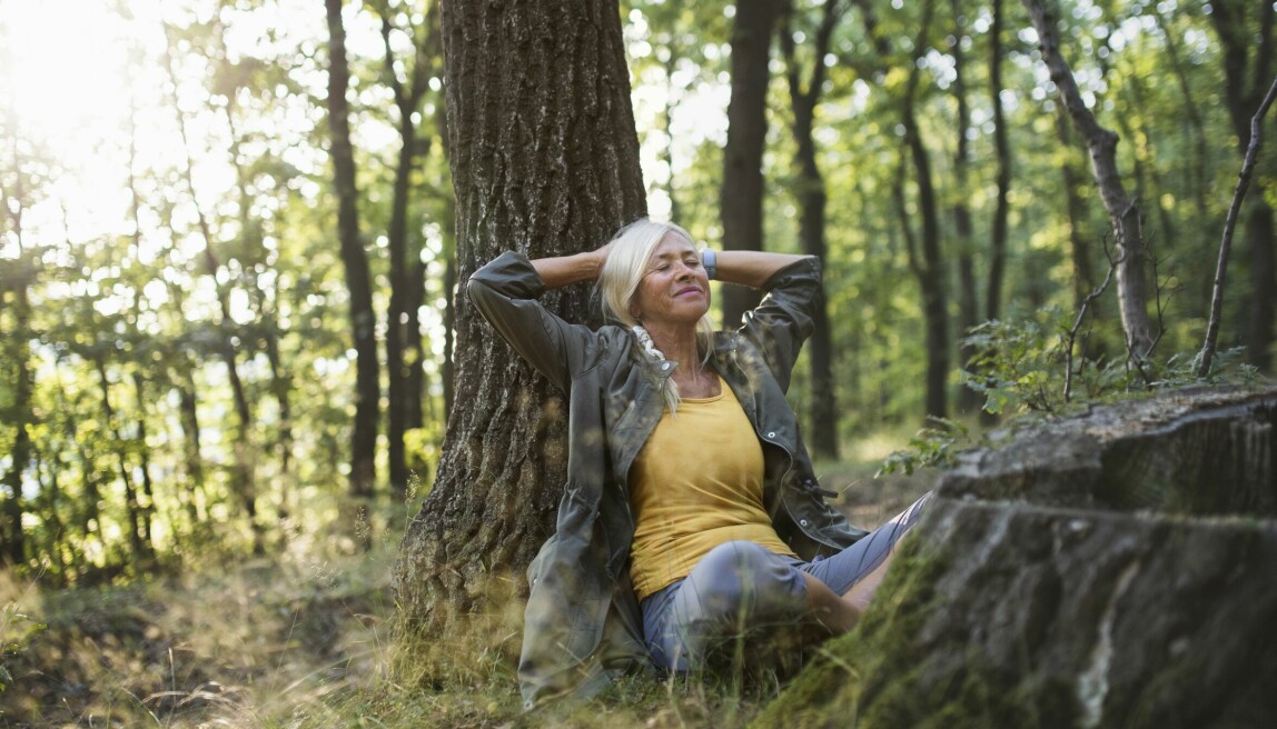 Kvinna sitter lutad mot trädstam och blundar