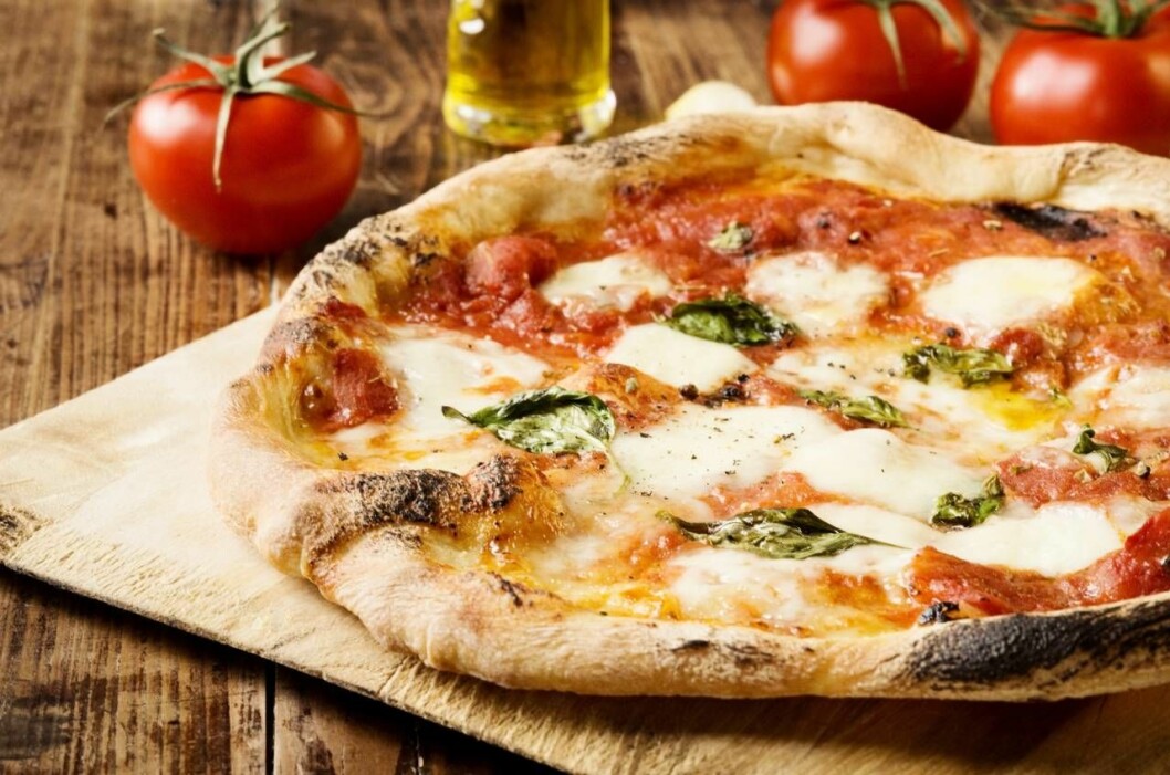 Pizza med tomater i bakgrunden