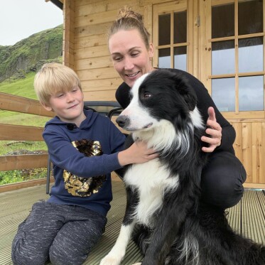 Christina vill visa Silas så mycket som möjligt av världen. Här besöker de Island tillsammans. Silas och Christina sitter på golvet på en veranda och klappar en svartvit hund under ett besök på Island