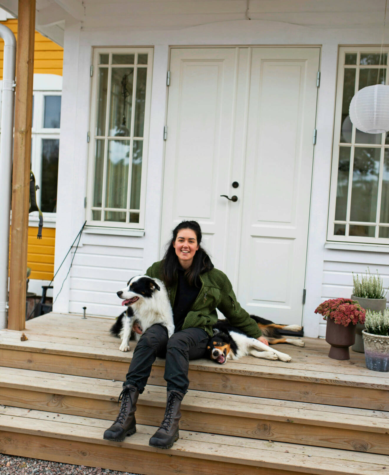 Sofie sitter på sin trappa ute vid dörren till sitt hus, håller om sina två hundar.