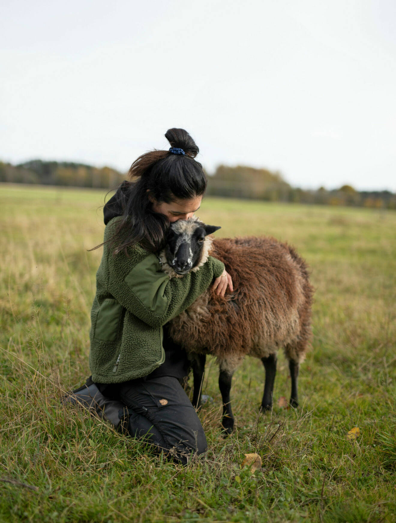 Sofie med tofs i håret, kramar om ett brunt får.