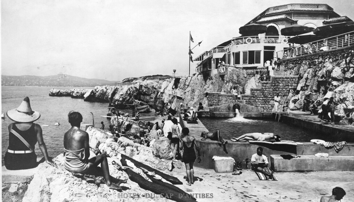 Jack tog Gunilla till Hotel du Cap Eden-Roc som ligger vid havet. Solbadande människor har samlats på klippor och bryggor vid Hotel du Cap Eden-Roc på Franska rivieran.