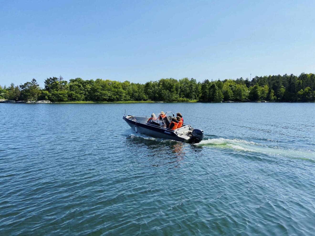 Tre personer med flytvästar åker på en motorbåt till havs i somrigt väder.