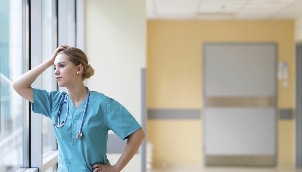 Trött sjuksköterska står lutan mot en fönsterruta
