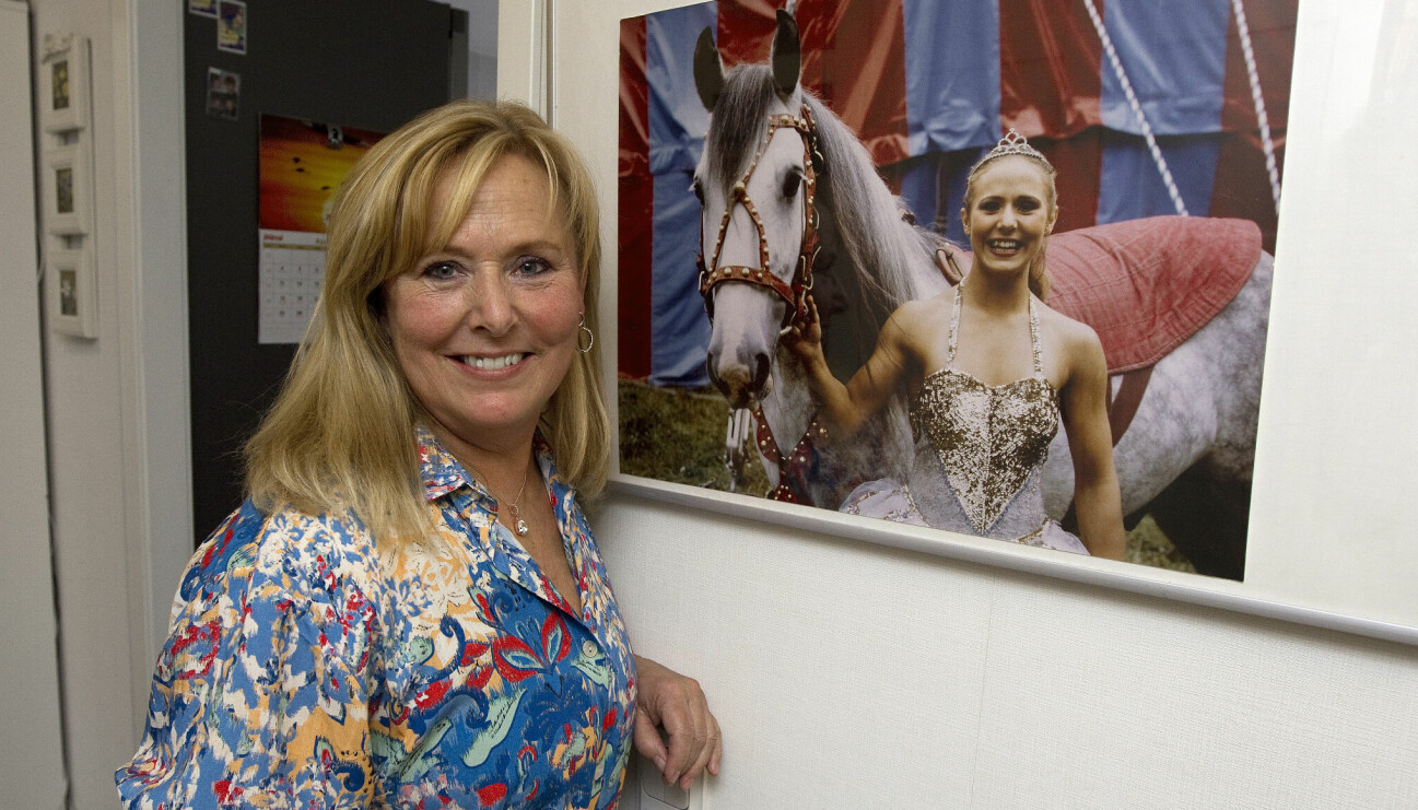 Susanne står brevid ett foto av sig själv som ung iklädd glittrig scenklädsel och tiara i håret där hon håller en häst i grimman och berättar om hur hon som 14-åring hoppade av skolan för att börja jobba på cirkus.