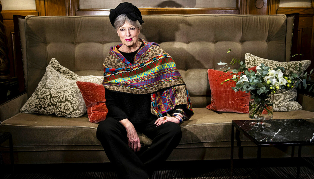 Suzanne Brogger sitter i en soffa iklädd en mönstrad scarf och svart turban