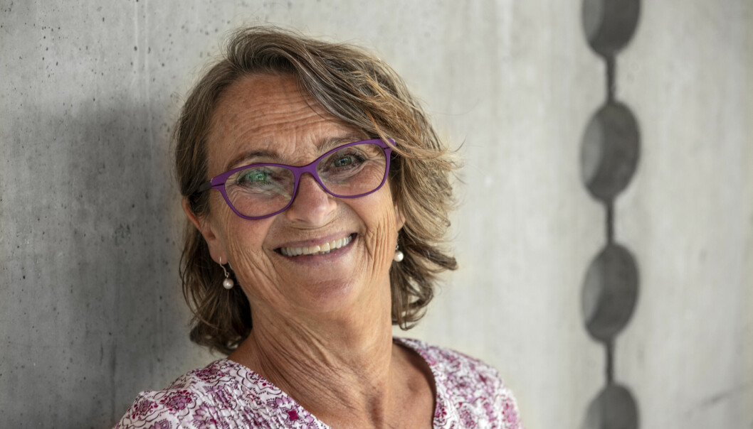 Skådespelerskan Suzanne Reuter står lutad mot en betongvägg. Hon ler och tittar in i kameran. Hon är klädd i en blommig blus eller klänning och har ett par lila glasögon.