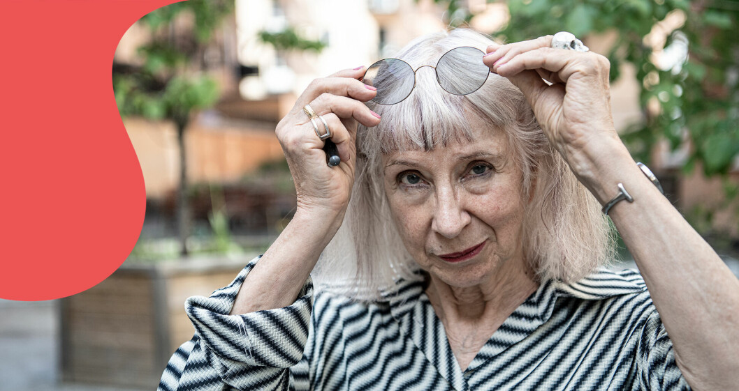 Suzanne Osten står i en trädgård och tittar in i kameran med solglasögonen på huvudet.