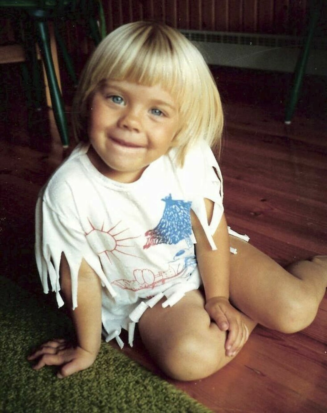 Therése Lindgren som liten flicka, sittande på golvet iförd en t-shirt med hemma-målat motiv och klippta fransar.