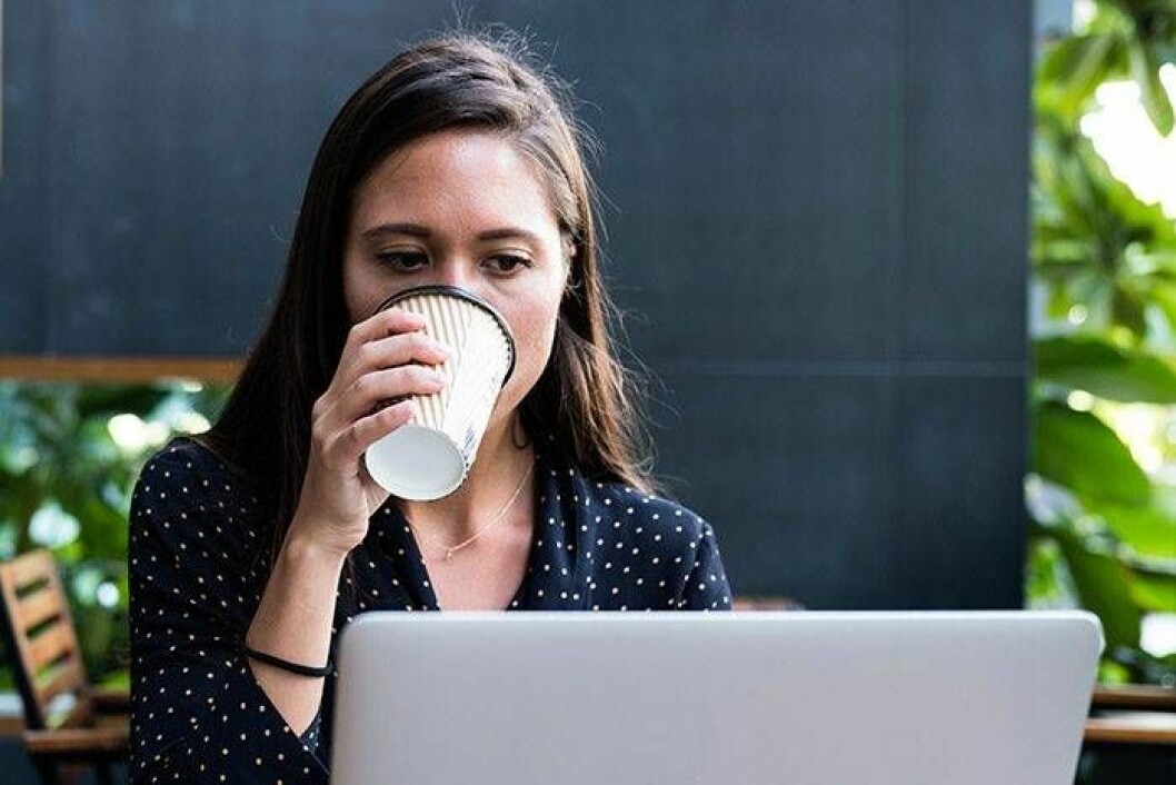 tjej dricker ur en kopp, sitter framför en dator och ser koncentrerad ut