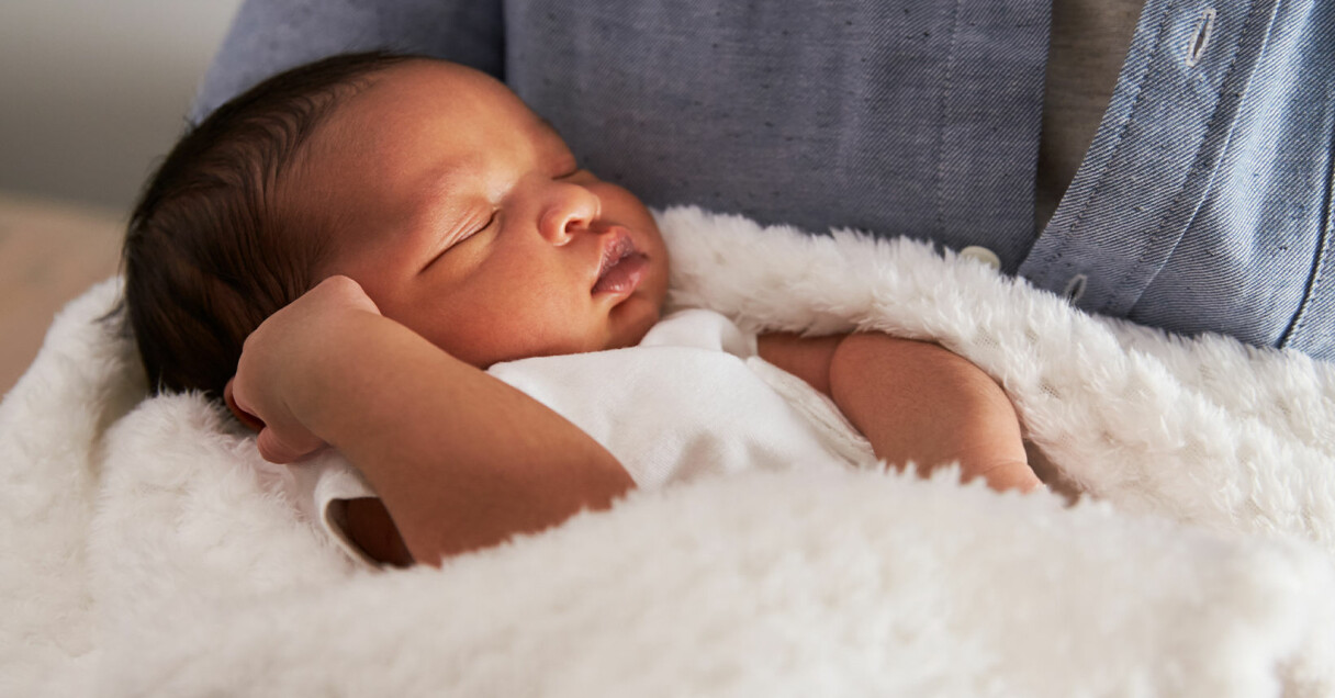 en bebis i vit body ligger i en vit filt och blundar