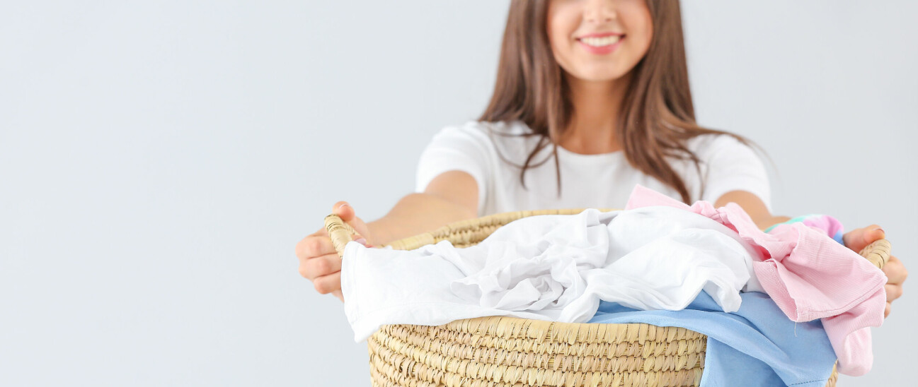 Kvinna med ett leende som håller upp en tvättkorg fylld med tvätt.