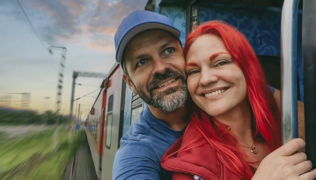 Sedan 1 september har makarna varit på resa genom Indien, här på en 46 timmar lång tågresa från New Delhi i norr till Kerala i söder. Anders och Lousie lutar sig ut från ett tågfönster under en resa. Mannen har blå tröja och keps på sig. Kvinnan har rött hår, ögonbryn och tröja.