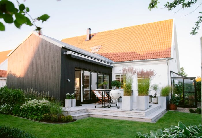 När familjen Tidstrand behövde mer plats blev det en svart tillbyggnad som bryter helt mot den vita villan. Den omges av två trädäck som förbinds med en "brygga" på kortsidan bakom rabatten. Tillbyggnaden på familjens hus.