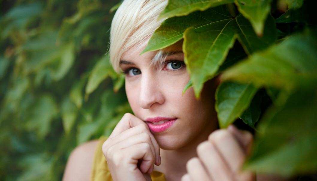 Ung kvinna med kort, blond frisyr, framför murgröna.