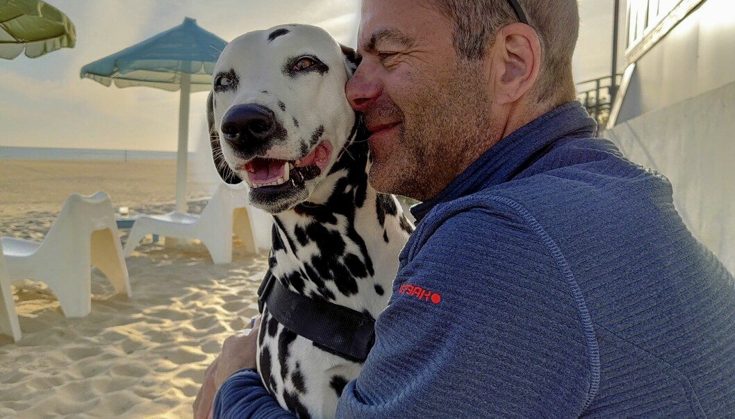 Urban sitter utan för din husbil på en strand och håller om sin hund Emmi.