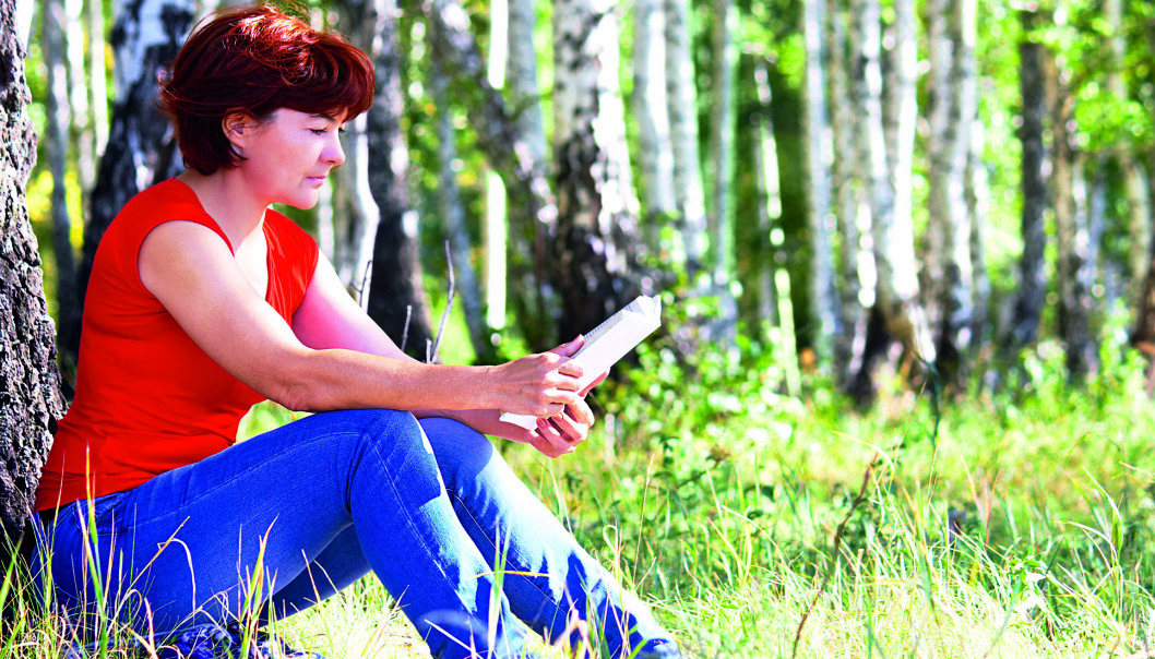 Kvinna sitter och läser i gräset