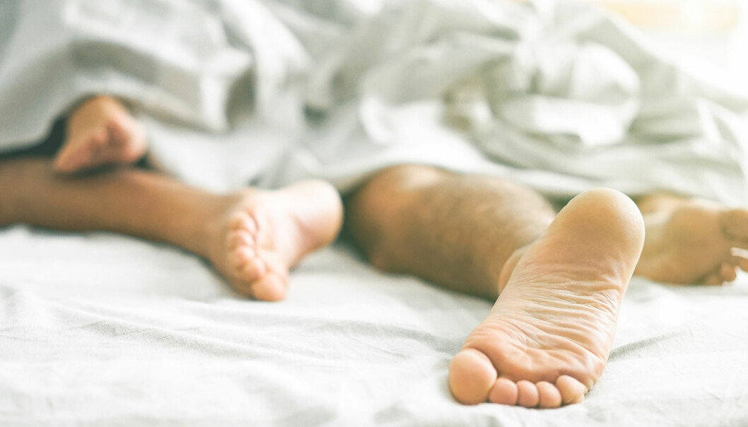 Ett par ligger tätt omslingrade i en säng. VI ser bara fötterna.