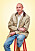 Artisten Petter sitter på en röd pall. Han är klädd i beige jacka, ljus skjorta och jeans.