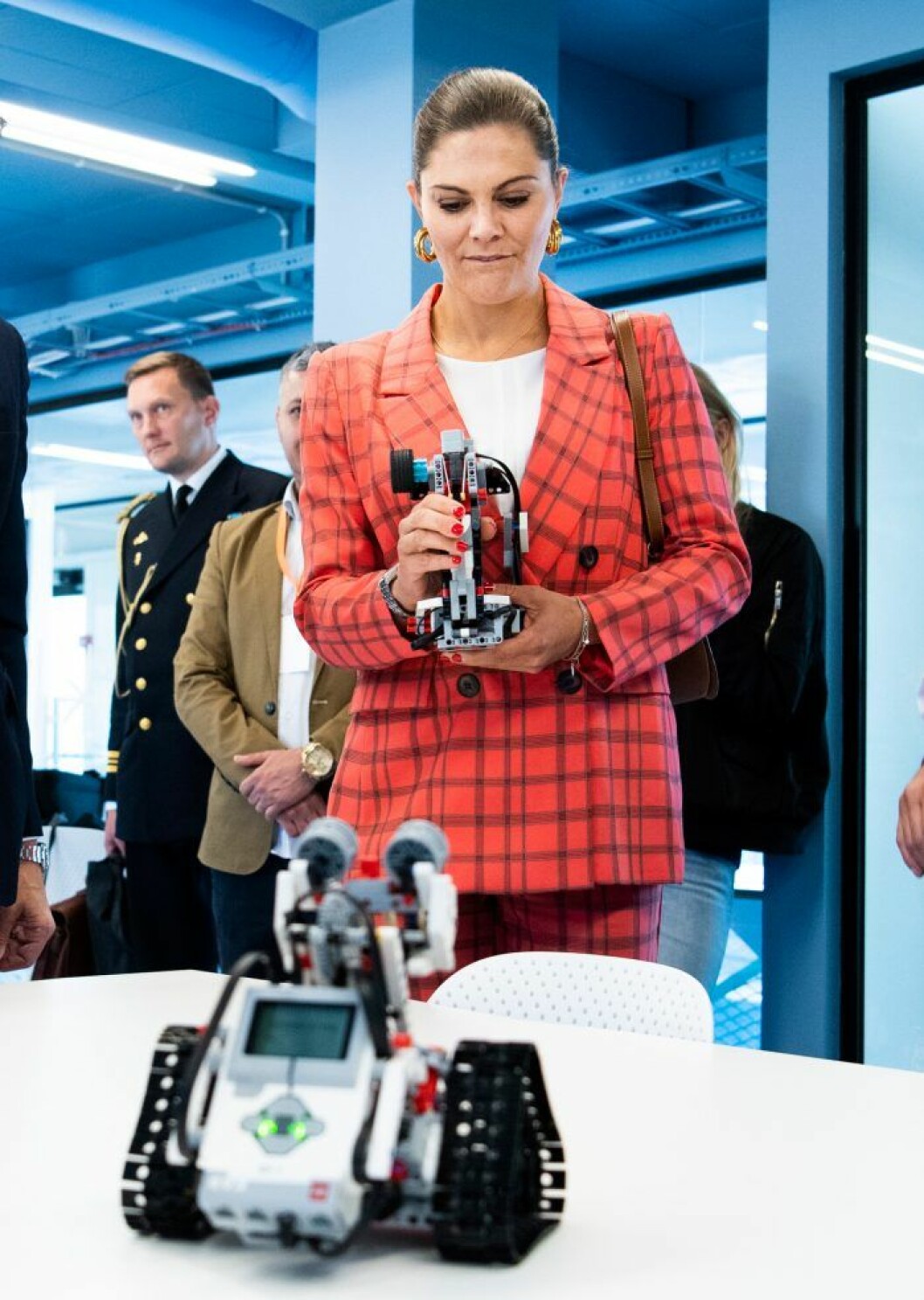 Undrar du över mannen i uniform? Det är vakthavande adjutant som skymtar i bakgrunden. Kronprinsessan Victoria prins Daniel testar att köra robot under ett arbetsuppdrag.