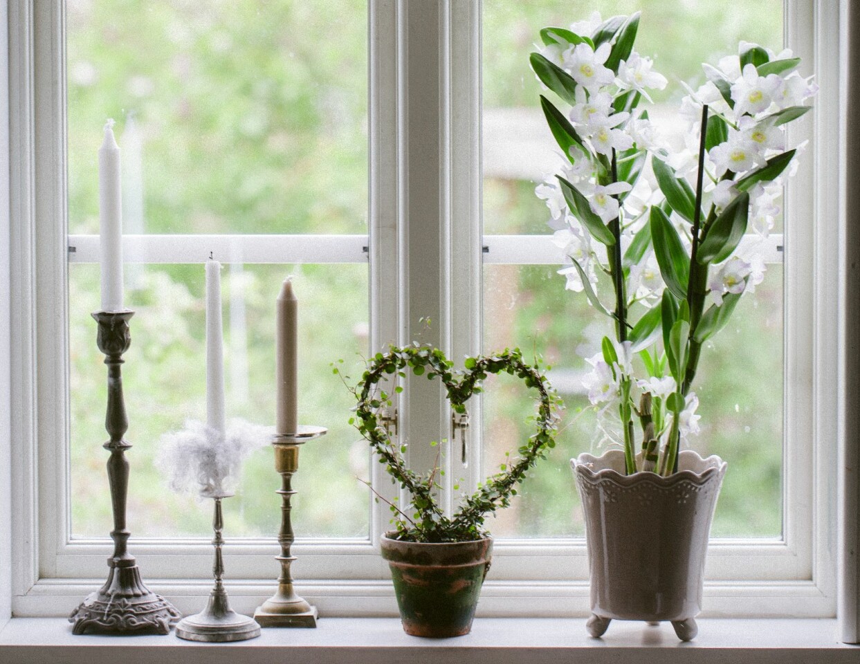 Vit orkidé i fönsterkarm tillsammans med ljus och slingeranka på båge.