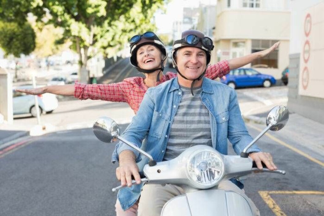 Par åker vespa på solig väg i stad.